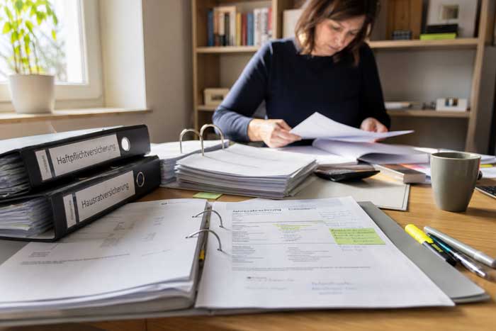 Eine Frau vergleicht sämtliche Versicherungsunterlagen zuhause
